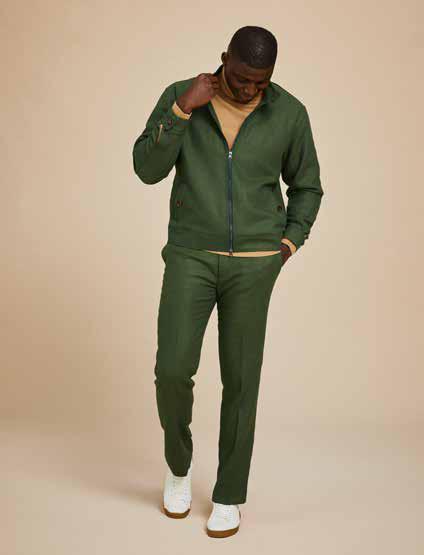 An individual wearing the Inserch Olive Wool Blend Herringbone Jacket (JS263-19) is seen paired with blue jeans and brown sneakers, standing against a beige background.