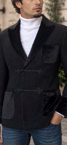 A man wears a black Insomnia MANZINI MZW-556 Fancy Velvet Trim Sport Coat in a tailored fit with velvet trim, toggle closures, and patch pockets over a white turtleneck.