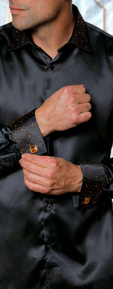 A man adjusts the cuff of the INSOMNIA IN-118 Slim Fit Satin Stone Collar & Cuff Black Gold Shirt by Insomnia, featuring gold studs on French cuffs and stone collar with amber-colored cufflinks.