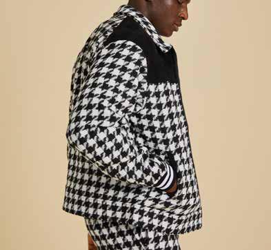 An individual with a beard stands against a beige background, donning an Inserch Wool Blend Houndstooth Full Zip Bomber Jacket JS264-41 in black and white. The jacket's 2-way zipper and regular fit layer stylishly over his red shirt, blue jeans, and white sneakers.