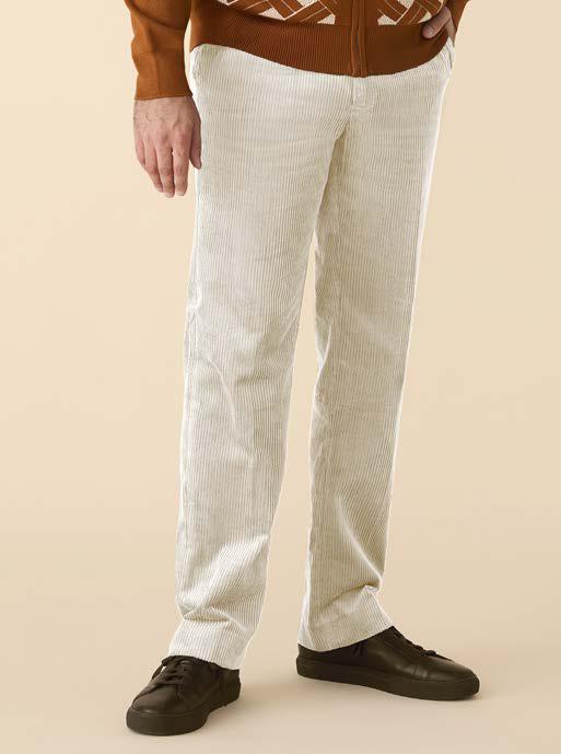 A person wearing Inserch Cotton Corduroy Pants P3103-134 Bone, a brown sweater, and black shoes stands against a beige background.