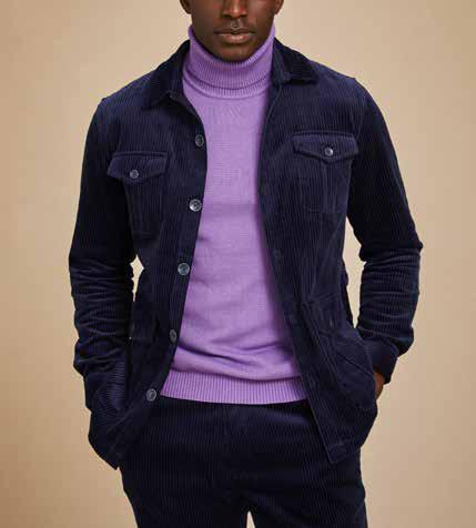 A person wearing the Inserch 4-Pocket Cord Jacket BL267-11 in navy, crafted from modern corduroy fabric made of 100% cotton, paired with an orange and blue patterned sweater underneath. Their hands are in their pockets against a beige background.