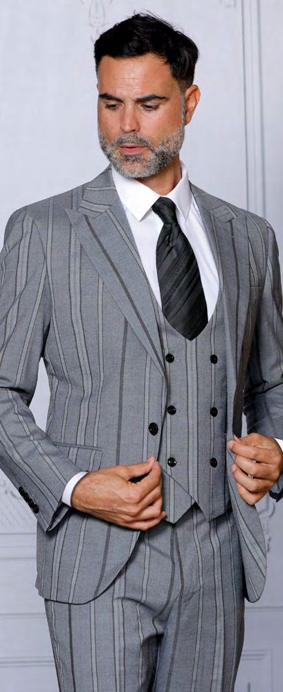 A man in an INSOMNIA ITALIA 3PC Tailored fit Dark Grey Suit by Insomnia, complemented by a white shirt and dark striped tie, stands against a light backdrop while adjusting his jacket.