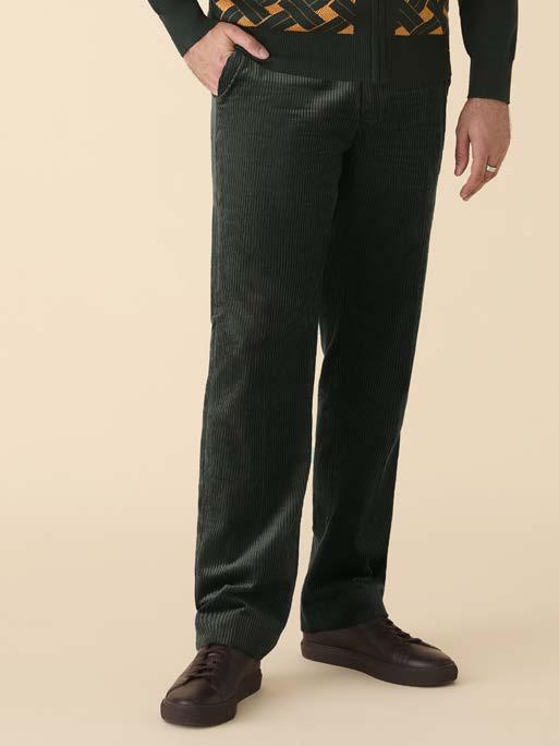 A man stands against a beige background wearing a green and yellow patterned zip-up jacket, mustard shirt, Inserch Cotton Corduroy Pants P3103-21 Hunter Green by Inserch, and brown shoes.