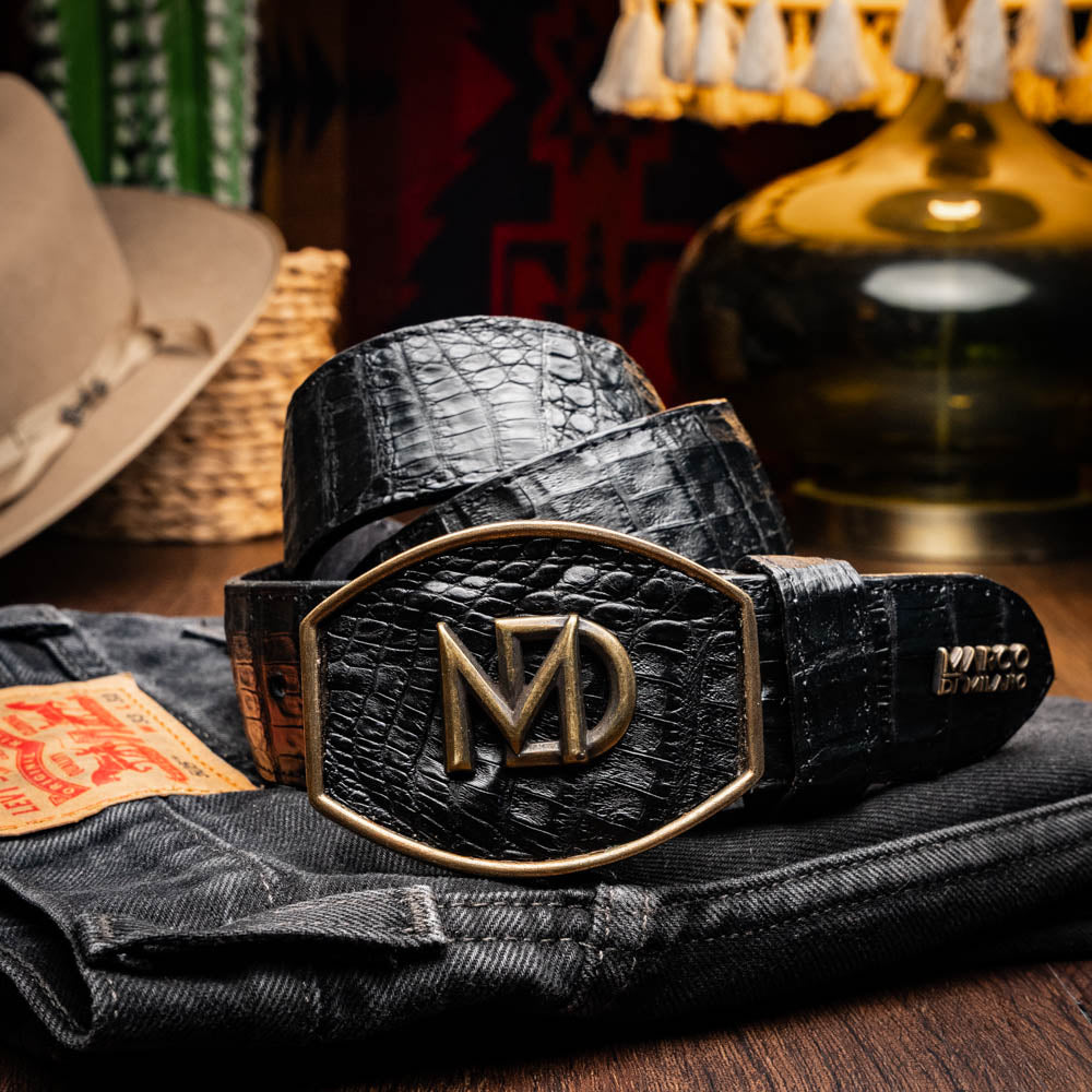 The Iowa Belt Black by Marco Di Milano is crafted from genuine black caiman skin with a crocodile texture, featuring a bold gold "MD" buckle and embossed branding—an eye-catching Western belt for any outfit.