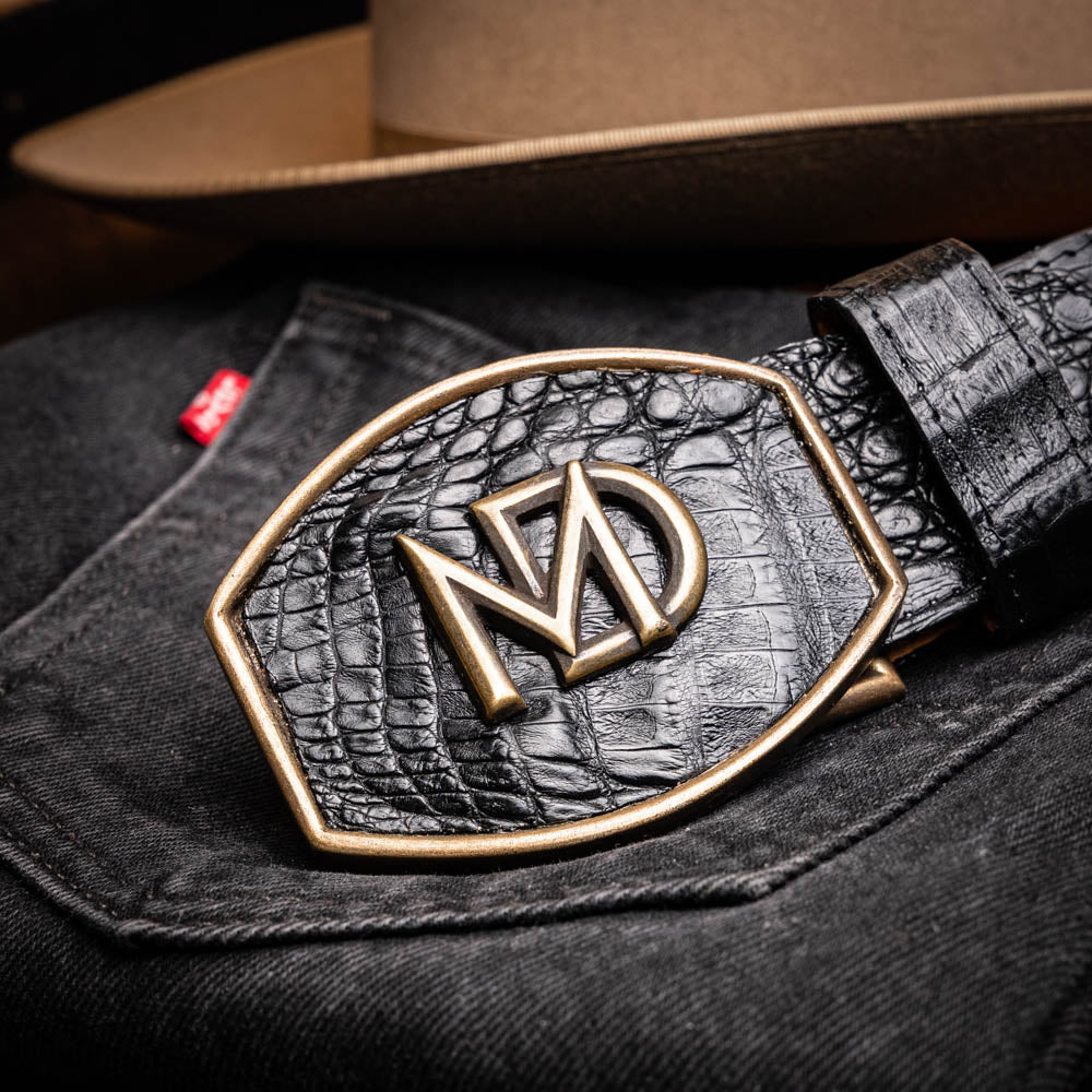The Iowa Belt Black by Marco Di Milano is crafted from genuine black caiman skin with a crocodile texture, featuring a bold gold "MD" buckle and embossed branding—an eye-catching Western belt for any outfit.
