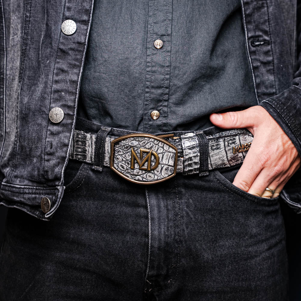 The Marco Di Milano Iowa Belt Stone Gray features genuine caiman skin and a bold gold "MD" buckle on a textured background, combining luxury with standout Western style.
