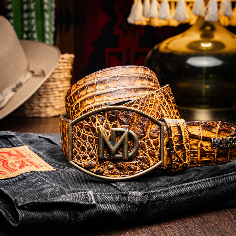 The Iowa Belt Mustard Brown by Marco Di Milano features genuine caiman crocodile leather and a bold gold "MD" buckle, elegantly displayed on a white background—showcasing the brand's signature luxury style.
