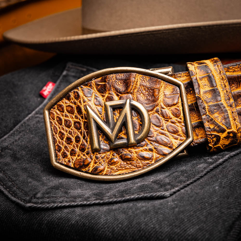 The Iowa Belt Mustard Brown by Marco Di Milano features genuine caiman crocodile leather and a bold gold "MD" buckle, elegantly displayed on a white background—showcasing the brand's signature luxury style.