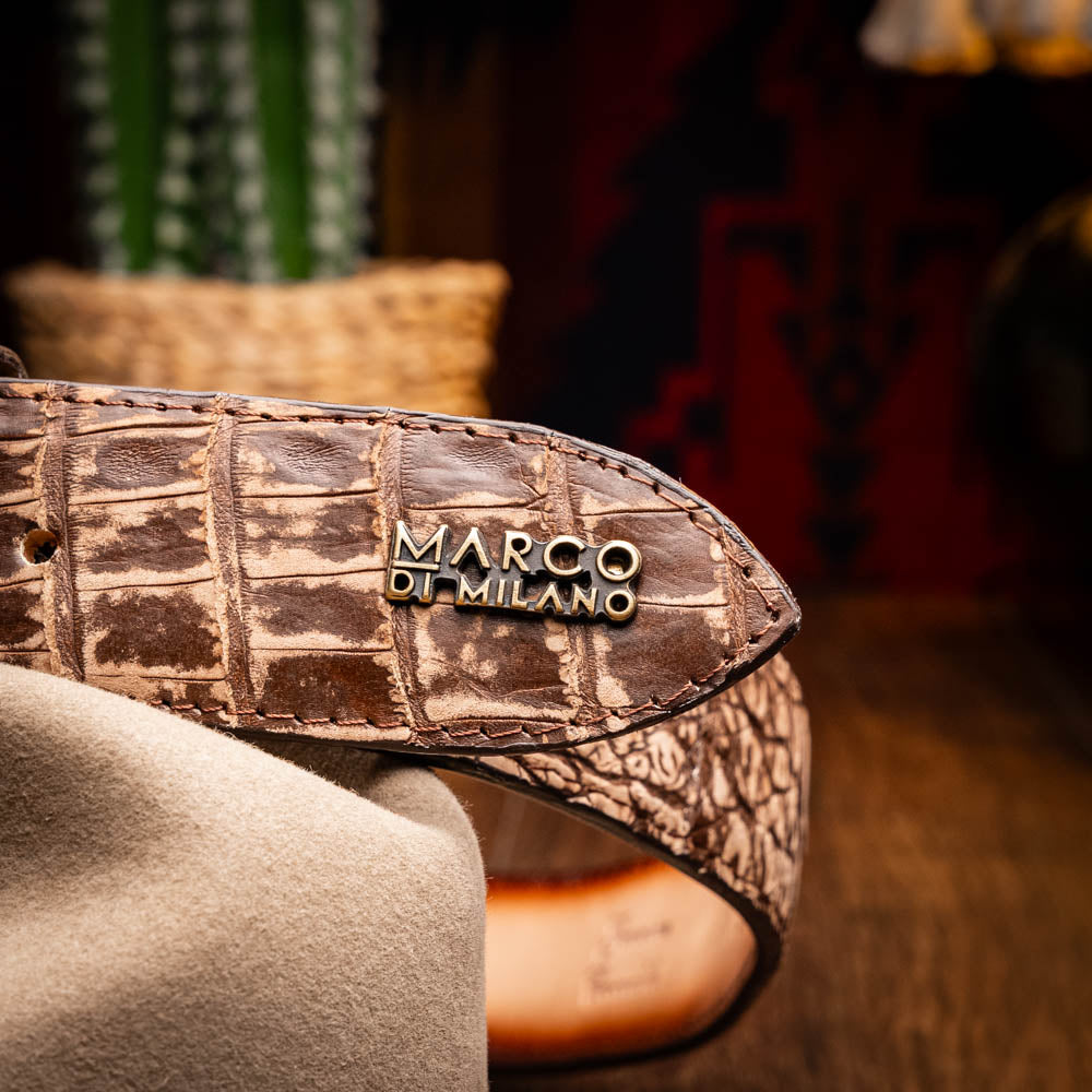 The Marco Di Milano Iowa Belt Stone Brown features genuine caiman crocodile leather, a gold "MD" buckle, and "Marco Milano" engraved on the side, evoking a classic western style against a white background.