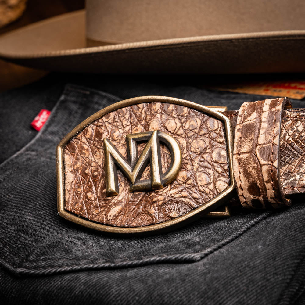 The Marco Di Milano Iowa Belt Stone Brown features genuine caiman crocodile leather, a gold "MD" buckle, and "Marco Milano" engraved on the side, evoking a classic western style against a white background.