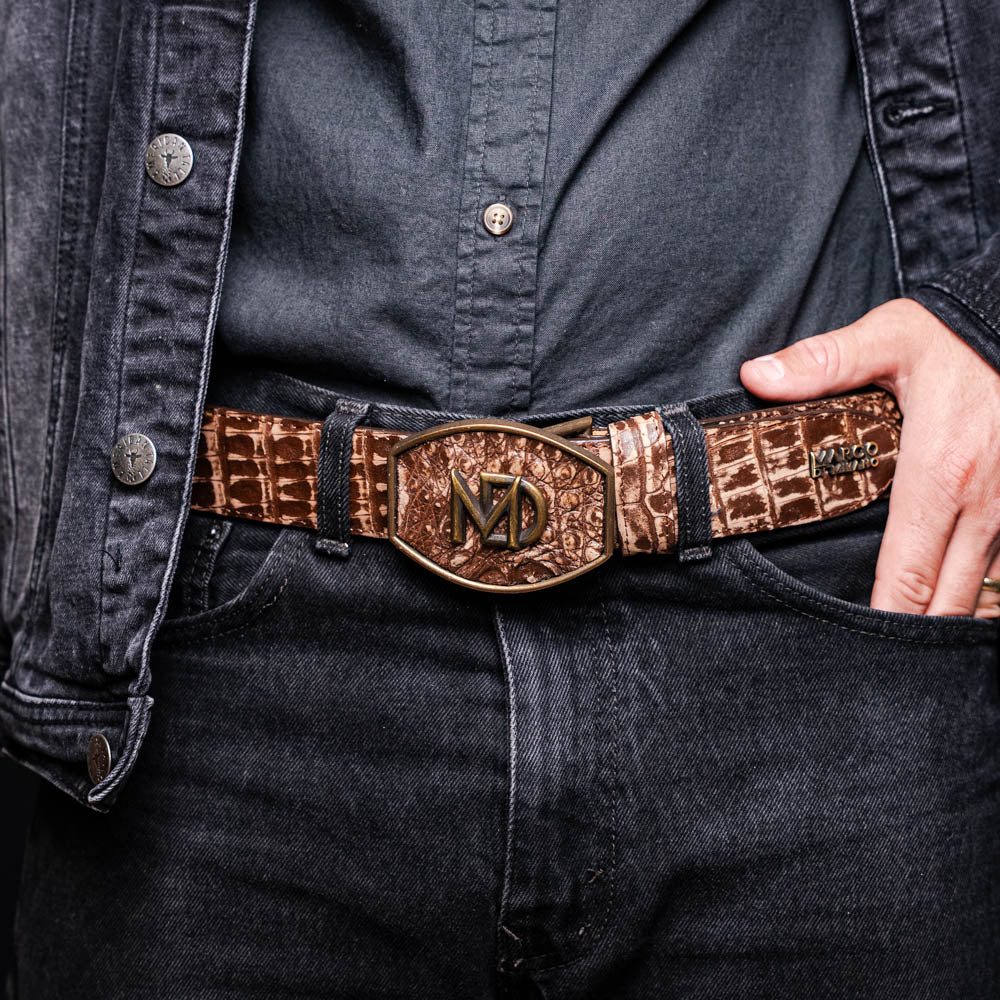 The Marco Di Milano Iowa Belt Stone Brown features genuine caiman crocodile leather, a gold "MD" buckle, and "Marco Milano" engraved on the side, evoking a classic western style against a white background.