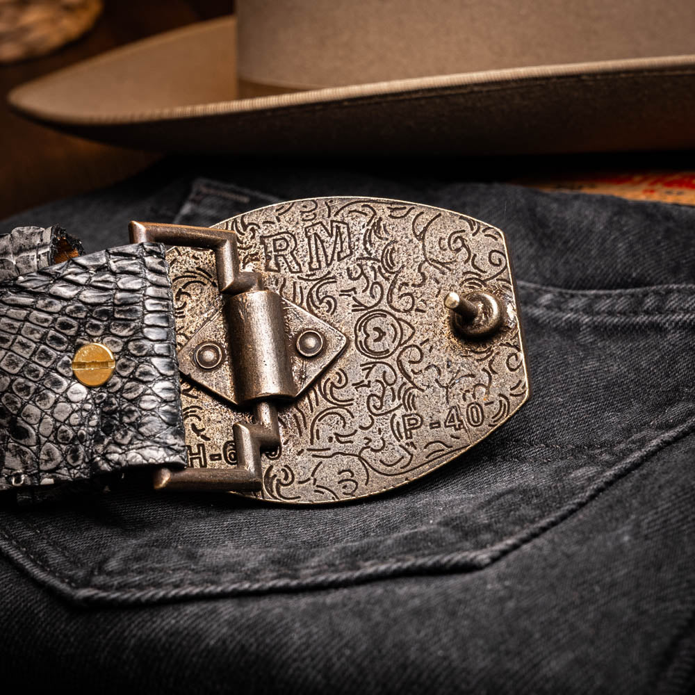 The Marco Di Milano Iowa Belt Stone Gray features genuine caiman skin and a bold gold "MD" buckle on a textured background, combining luxury with standout Western style.