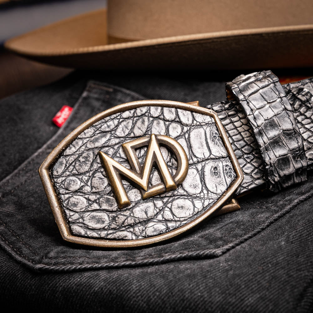The Marco Di Milano Iowa Belt Stone Gray features genuine caiman skin and a bold gold "MD" buckle on a textured background, combining luxury with standout Western style.