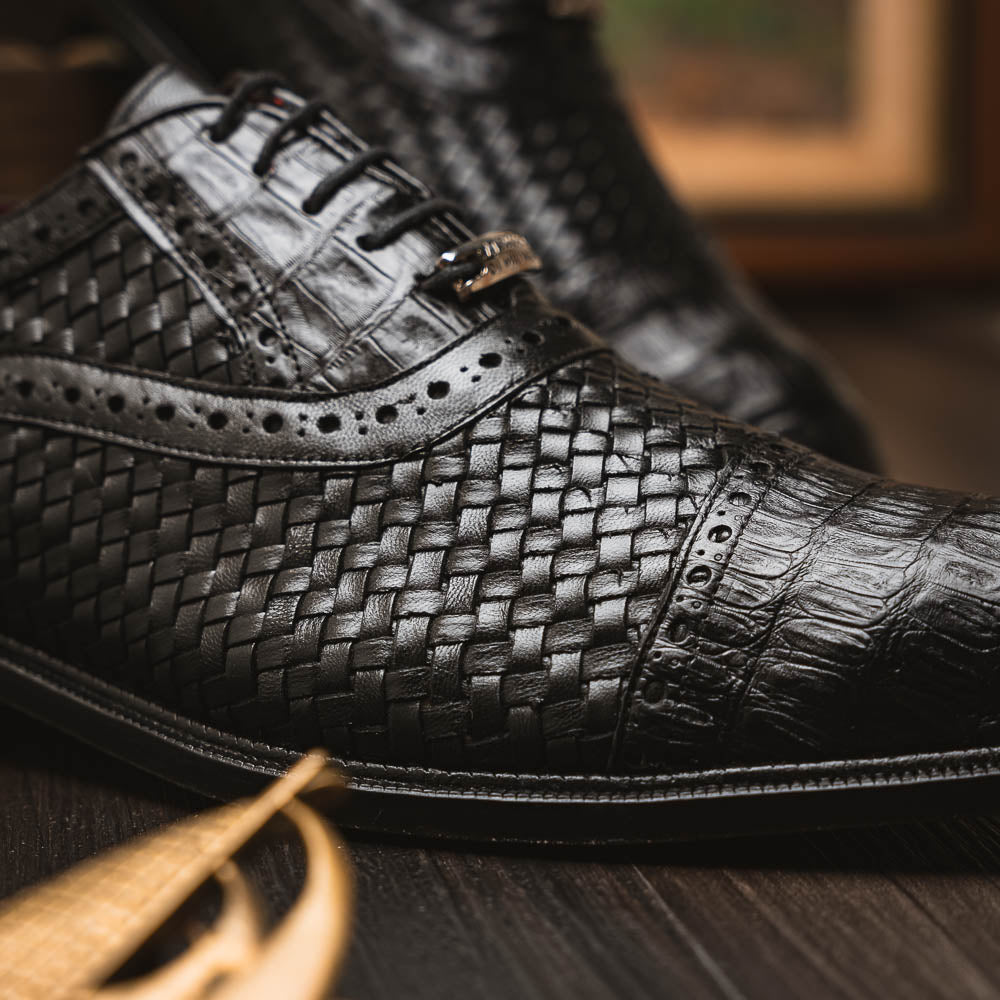 A pair of luxury "John Black" dress oxfords by Marco Di Milano, crafted from genuine caiman crocodile leather with intricate detailing and brown leather soles—one upright, the other resting sideways beneath it.