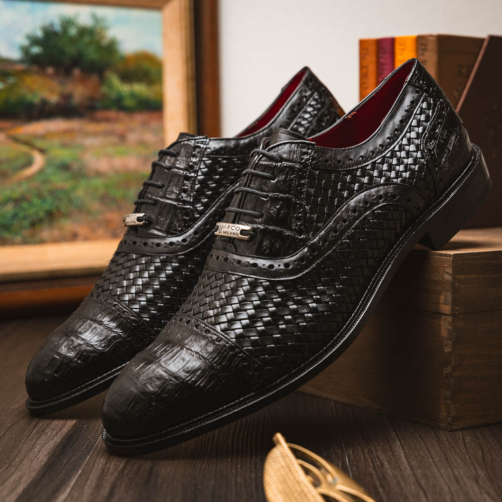 A pair of luxury "John Black" dress oxfords by Marco Di Milano, crafted from genuine caiman crocodile leather with intricate detailing and brown leather soles—one upright, the other resting sideways beneath it.