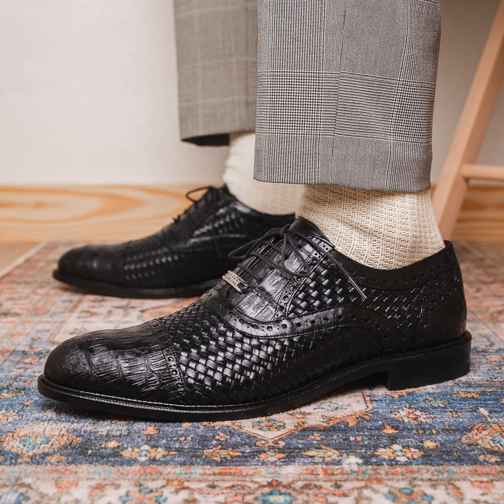 A pair of luxury "John Black" dress oxfords by Marco Di Milano, crafted from genuine caiman crocodile leather with intricate detailing and brown leather soles—one upright, the other resting sideways beneath it.