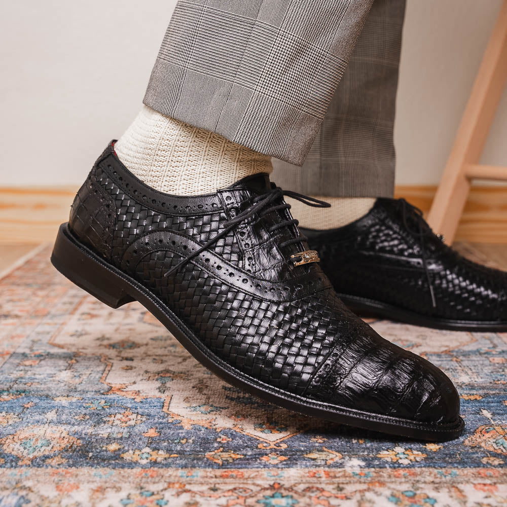 A pair of luxury "John Black" dress oxfords by Marco Di Milano, crafted from genuine caiman crocodile leather with intricate detailing and brown leather soles—one upright, the other resting sideways beneath it.