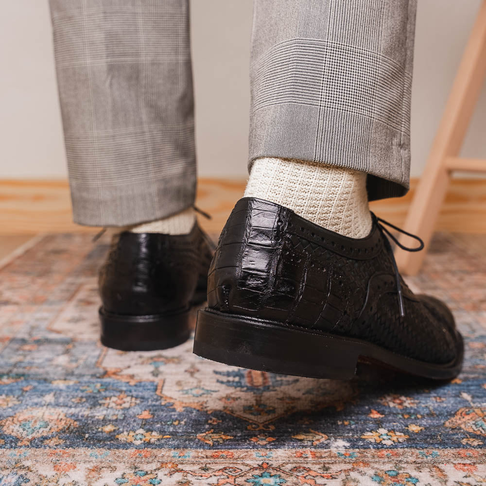 A pair of luxury "John Black" dress oxfords by Marco Di Milano, crafted from genuine caiman crocodile leather with intricate detailing and brown leather soles—one upright, the other resting sideways beneath it.