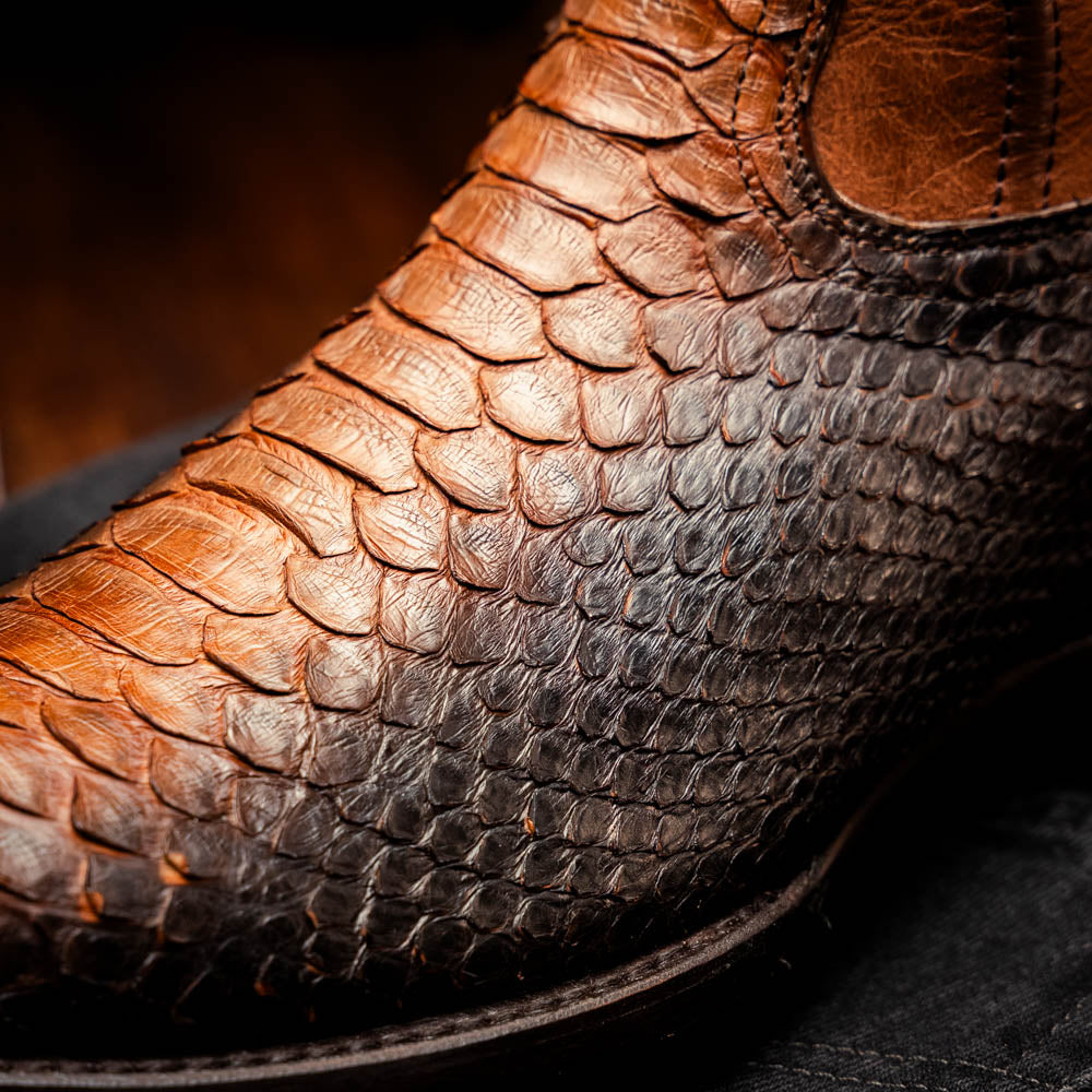 A pair of Kansas Lisboa boots by Marco Di Milano in brown and black python leather, featuring textured scales; one boot stands upright while the other displays the branded sole with "Marco Di Milano" text.
