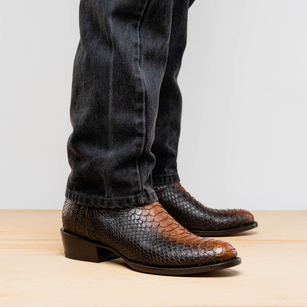 A pair of Kansas Lisboa boots by Marco Di Milano in brown and black python leather, featuring textured scales; one boot stands upright while the other displays the branded sole with "Marco Di Milano" text.