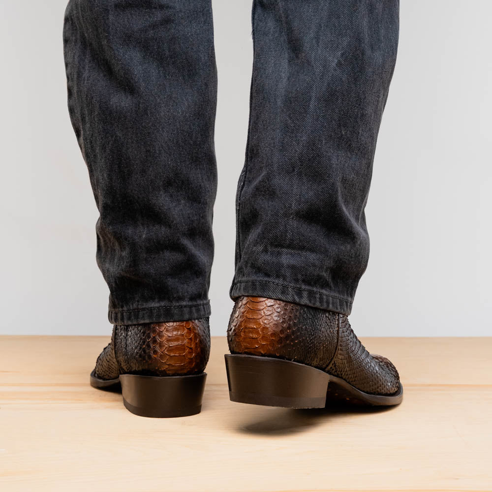 A pair of Kansas Lisboa boots by Marco Di Milano in brown and black python leather, featuring textured scales; one boot stands upright while the other displays the branded sole with "Marco Di Milano" text.