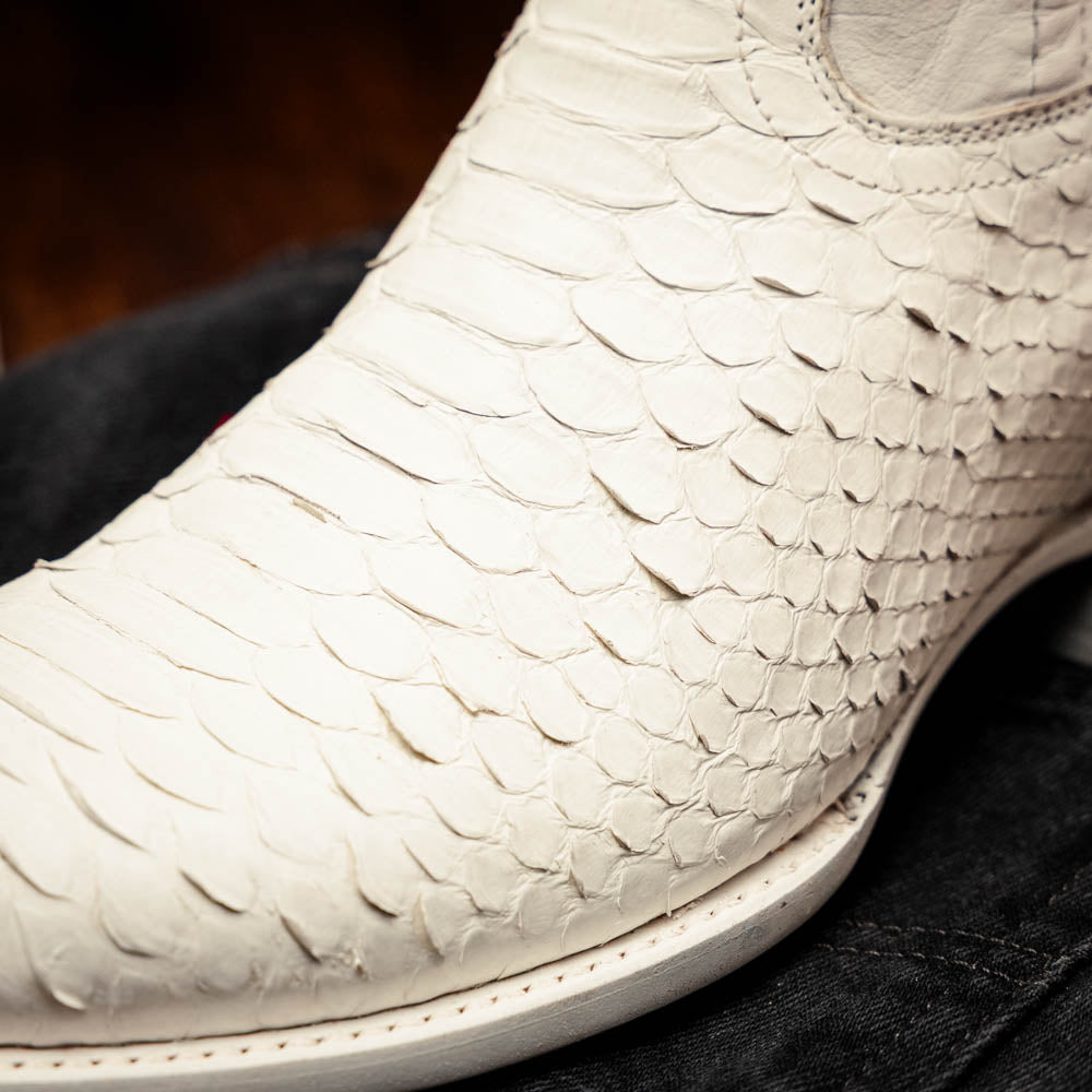 A pair of Kansas White cowboy boots by Marco Di Milano in white textured python skin with pointed toes and low heels; one boot stands upright while the other shows the branded sole.