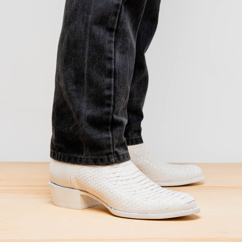 A pair of Kansas White cowboy boots by Marco Di Milano in white textured python skin with pointed toes and low heels; one boot stands upright while the other shows the branded sole.