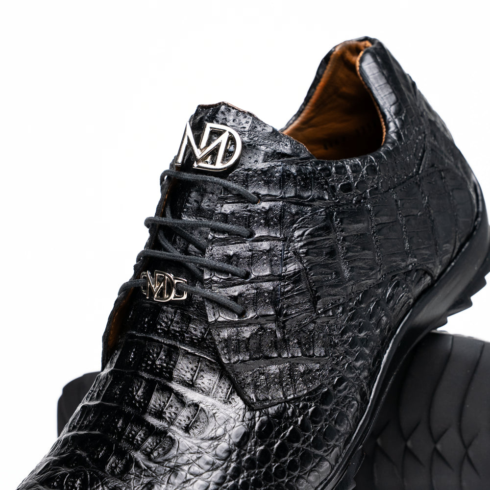 The Kratos Black by Marco Di Milano is a luxury black crocodile-patterned leather dress shoe, featuring a metal logo on the laces. Displayed with one upright and one on its side to showcase the detailed sole.
