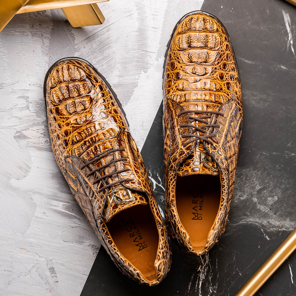 A pair of Kratos Rustic Orix brown crocodile-patterned leather dress shoes by Marco Di Milano, one upright and one tilted to display the textured sole, showcasing luxury footwear against a white background.