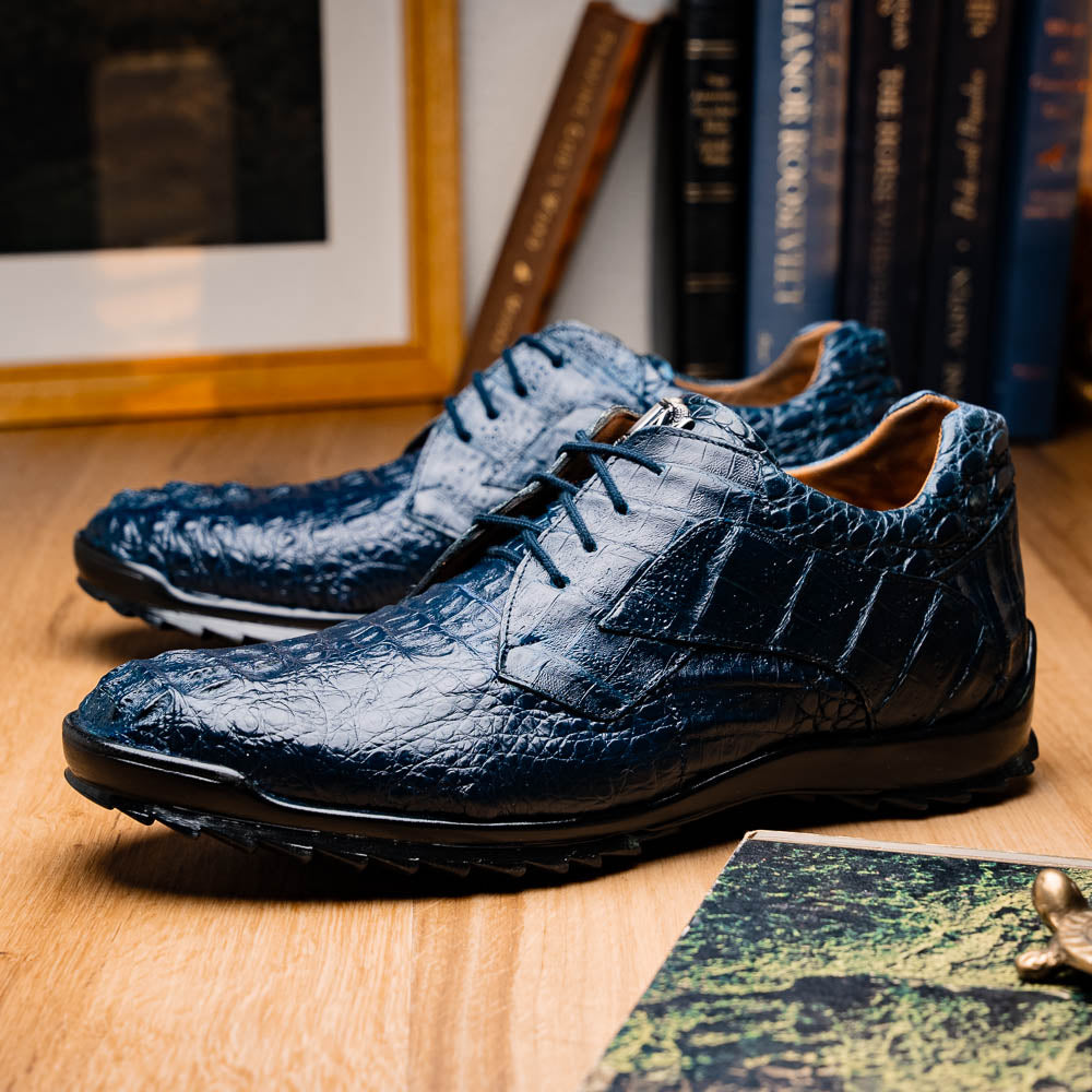 The Kratos Navy by Marco Di Milano: blue hand-painted crocodile-patterned leather dress shoes with black rubber soles—one upright, the other propped—a true statement of luxury footwear.
