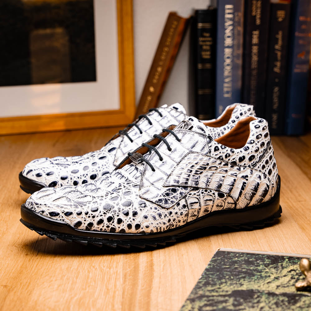 The Marco Di Milano Kratos Newspaper features white and black crocodile-patterned luxury dress shoes with black soles; one shoe stands upright, while the other lies on its side showcasing the hand-painted finish.