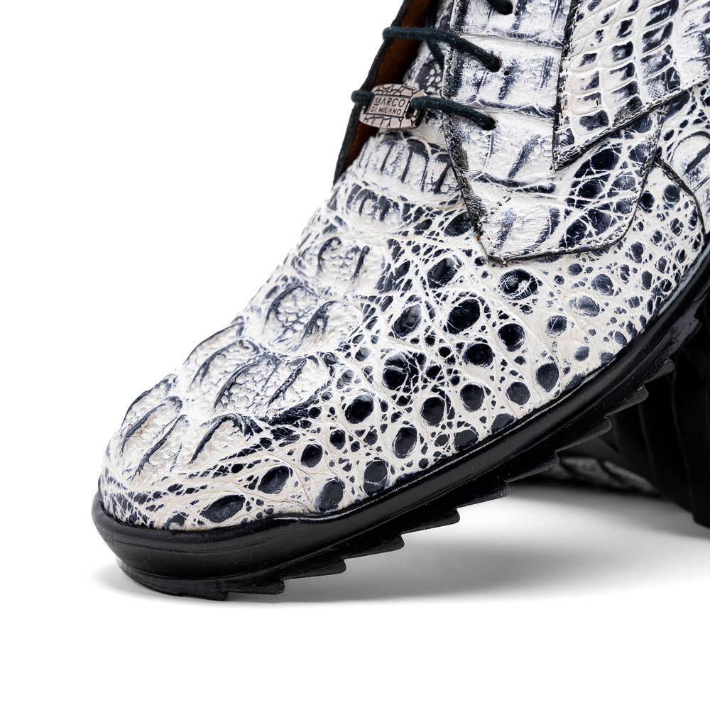 The Marco Di Milano Kratos Newspaper features white and black crocodile-patterned luxury dress shoes with black soles; one shoe stands upright, while the other lies on its side showcasing the hand-painted finish.