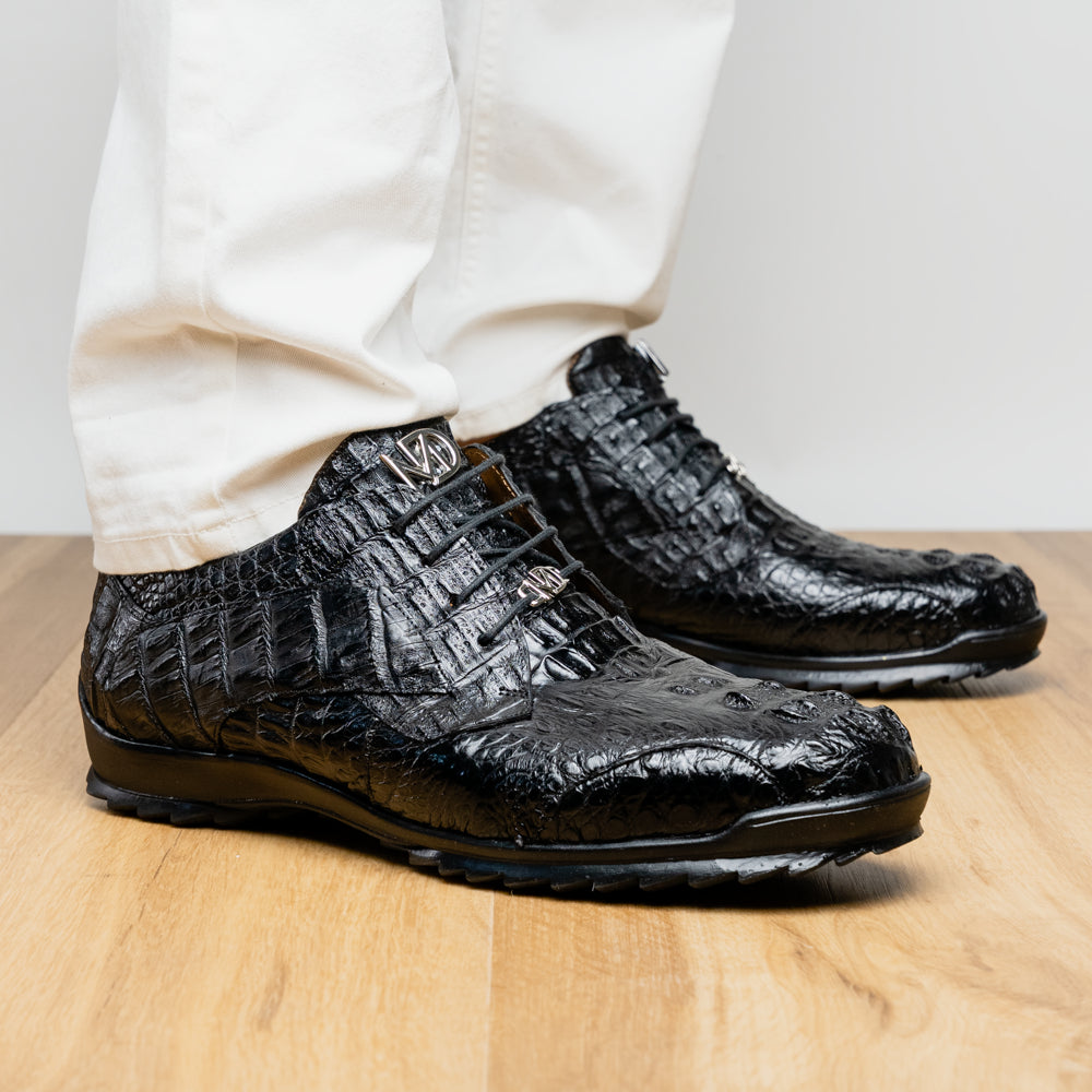 The Kratos Black by Marco Di Milano is a luxury black crocodile-patterned leather dress shoe, featuring a metal logo on the laces. Displayed with one upright and one on its side to showcase the detailed sole.