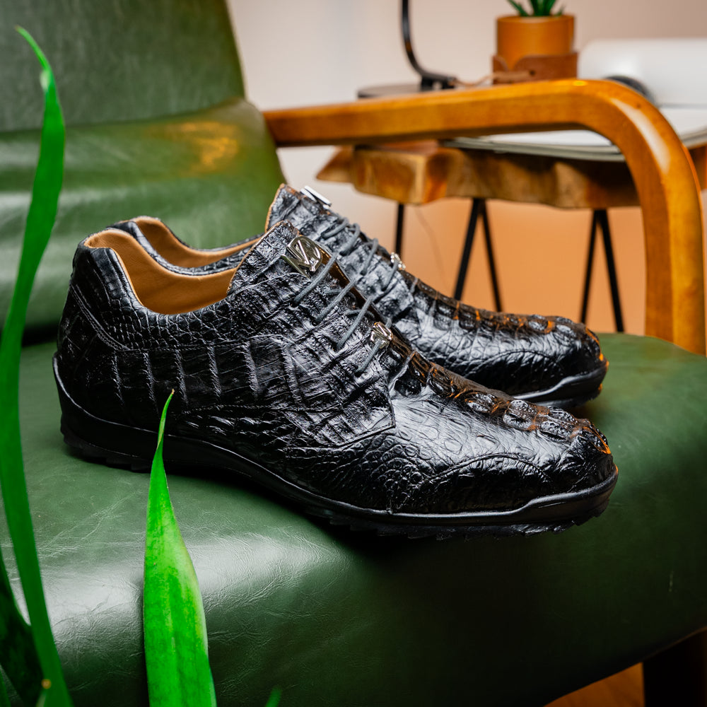 The Kratos Black by Marco Di Milano is a luxury black crocodile-patterned leather dress shoe, featuring a metal logo on the laces. Displayed with one upright and one on its side to showcase the detailed sole.