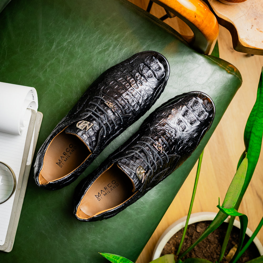 The Kratos Black by Marco Di Milano is a luxury black crocodile-patterned leather dress shoe, featuring a metal logo on the laces. Displayed with one upright and one on its side to showcase the detailed sole.