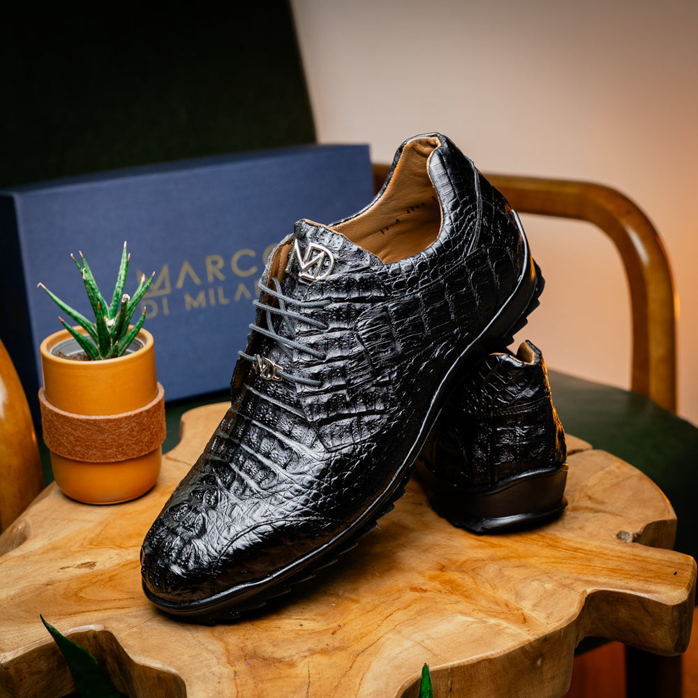 The Kratos Black by Marco Di Milano is a luxury black crocodile-patterned leather dress shoe, featuring a metal logo on the laces. Displayed with one upright and one on its side to showcase the detailed sole.