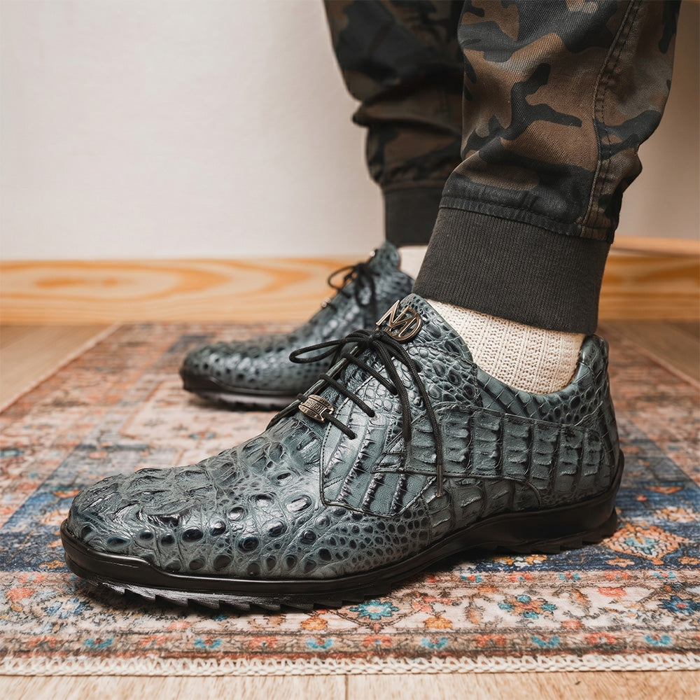 The Kratos Gray by Marco Di Milano are luxury dress shoes in textured gray crocodile-patterned leather with a hand-painted finish and black rubber soles; one shoe stands upright while the other rests on its side.