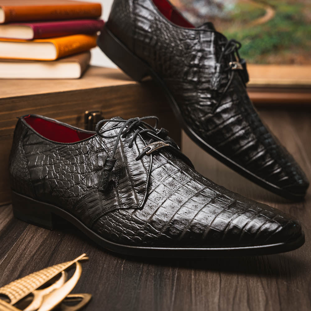 A pair of Marco Di Milano Lacio Black shoes—crafted from genuine caiman crocodile leather—one upright and one on its side, showing a brown leather sole embossed with luxury branding.