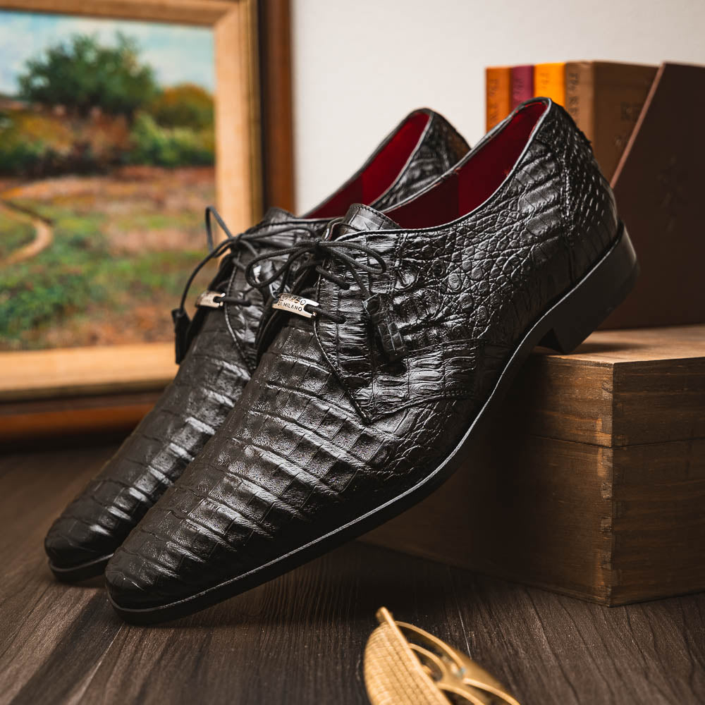 A pair of Marco Di Milano Lacio Black shoes—crafted from genuine caiman crocodile leather—one upright and one on its side, showing a brown leather sole embossed with luxury branding.