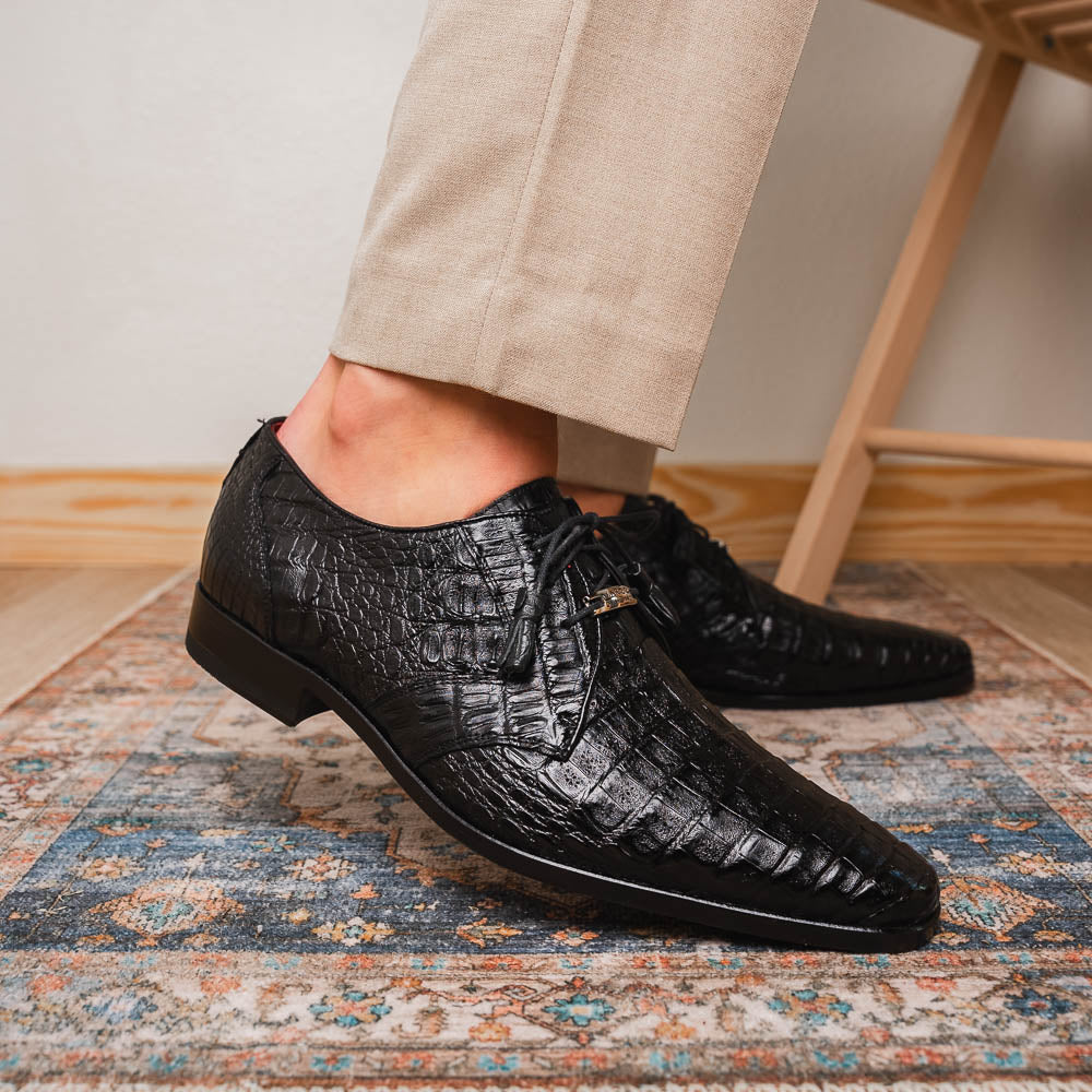 A pair of Marco Di Milano Lacio Black shoes—crafted from genuine caiman crocodile leather—one upright and one on its side, showing a brown leather sole embossed with luxury branding.