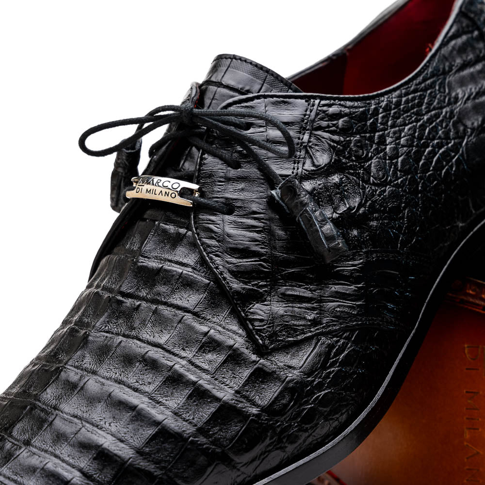 A pair of Marco Di Milano Lacio Black shoes—crafted from genuine caiman crocodile leather—one upright and one on its side, showing a brown leather sole embossed with luxury branding.