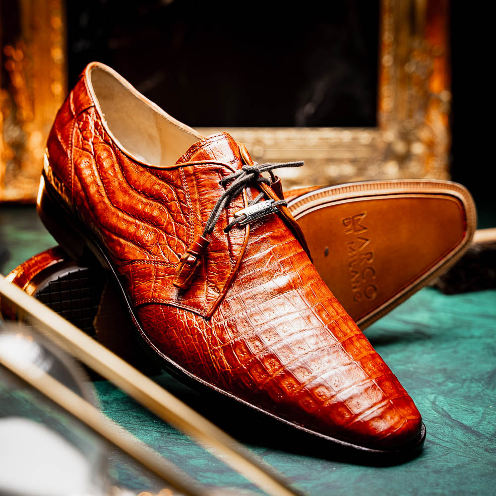 A pair of Marco Di Milano Lacio Brandy luxury derby shoes in a brown crocodile pattern, crafted from genuine caiman leather—one upright and one on its side to highlight the signature sole branding.