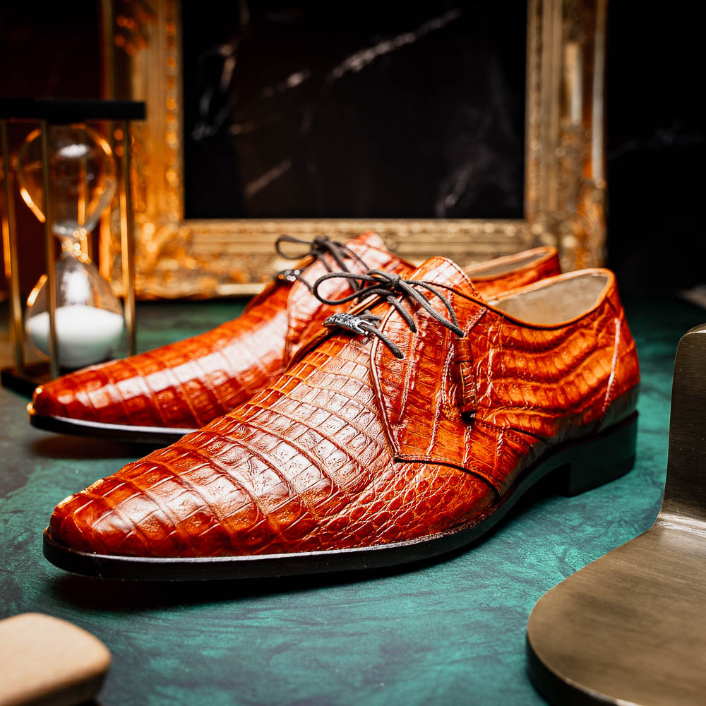 A pair of Marco Di Milano Lacio Brandy luxury derby shoes in a brown crocodile pattern, crafted from genuine caiman leather—one upright and one on its side to highlight the signature sole branding.