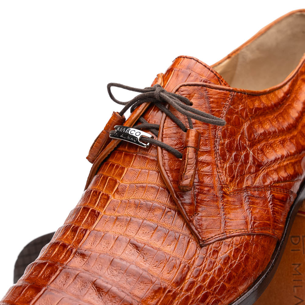 A pair of Marco Di Milano Lacio Brandy luxury derby shoes in a brown crocodile pattern, crafted from genuine caiman leather—one upright and one on its side to highlight the signature sole branding.