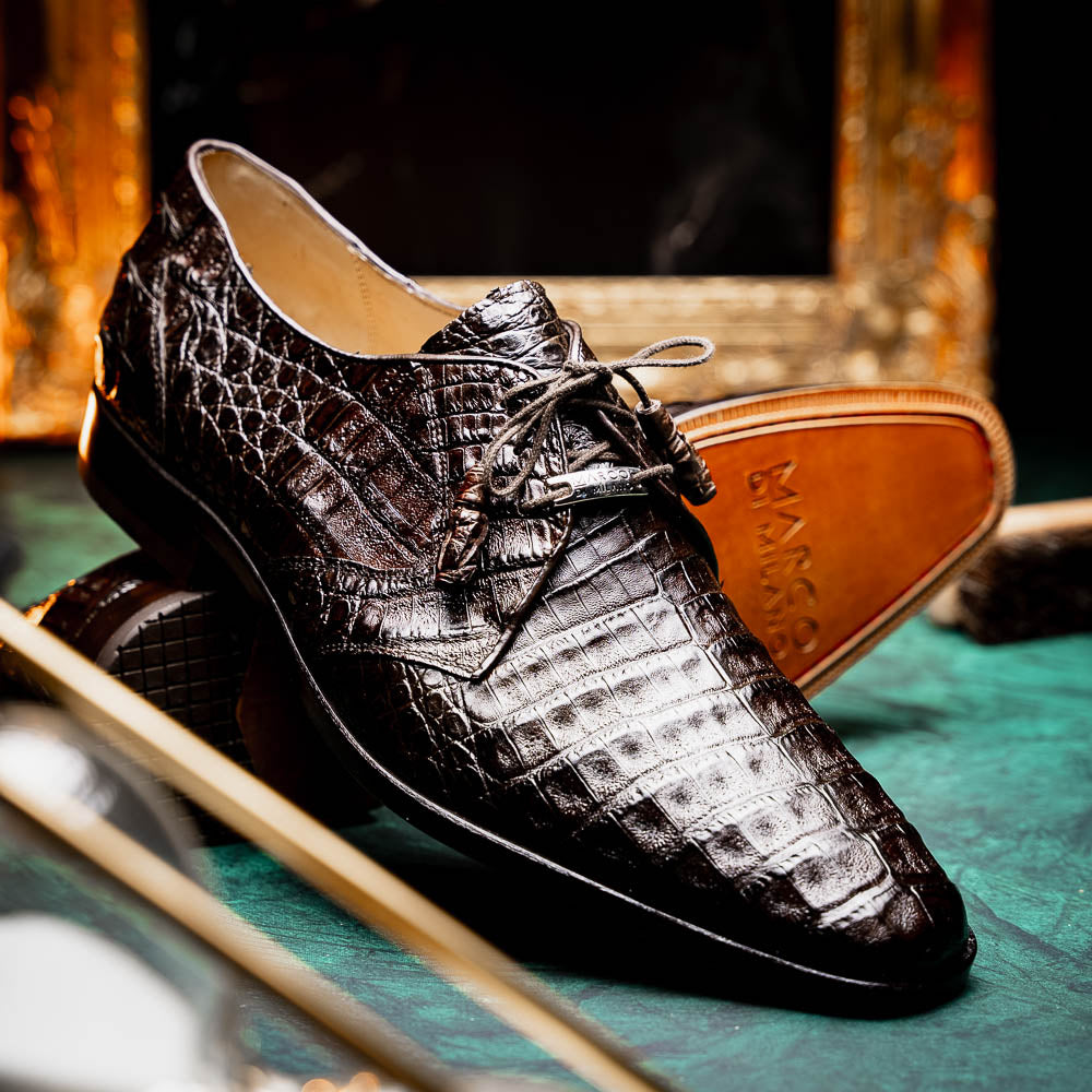 The "Lacio Brown" by Marco Di Milano is a luxury men's dress shoe made from genuine caiman crocodile leather, featuring tassel laces and the brand's logo—presented with one shoe resting atop the other.