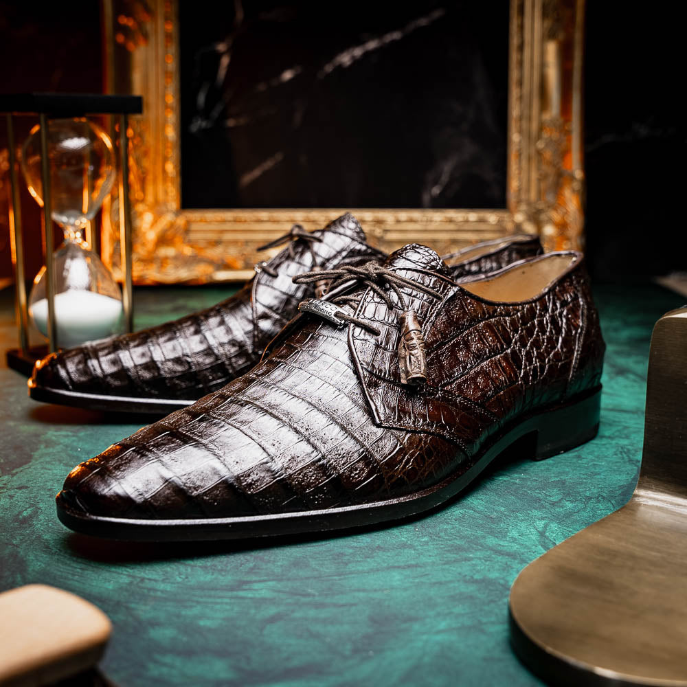 The "Lacio Brown" by Marco Di Milano is a luxury men's dress shoe made from genuine caiman crocodile leather, featuring tassel laces and the brand's logo—presented with one shoe resting atop the other.