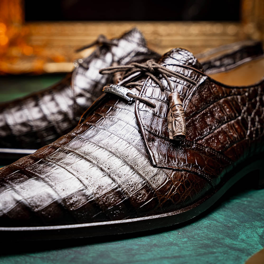 The "Lacio Brown" by Marco Di Milano is a luxury men's dress shoe made from genuine caiman crocodile leather, featuring tassel laces and the brand's logo—presented with one shoe resting atop the other.