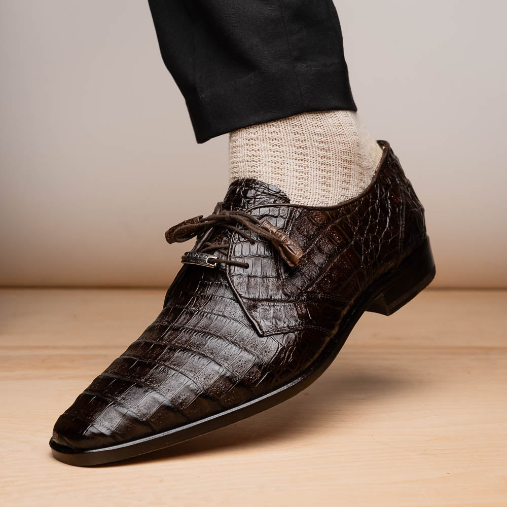 The "Lacio Brown" by Marco Di Milano is a luxury men's dress shoe made from genuine caiman crocodile leather, featuring tassel laces and the brand's logo—presented with one shoe resting atop the other.