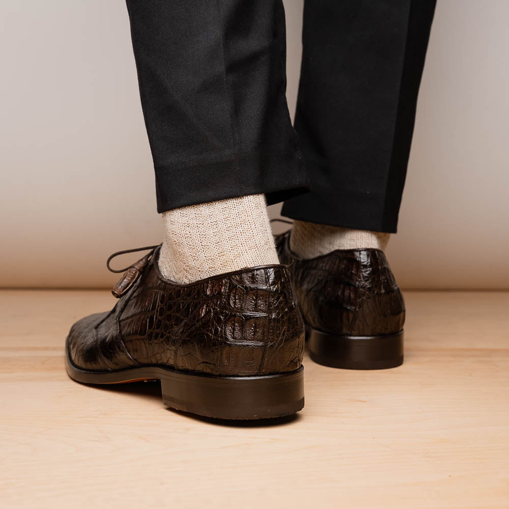 The "Lacio Brown" by Marco Di Milano is a luxury men's dress shoe made from genuine caiman crocodile leather, featuring tassel laces and the brand's logo—presented with one shoe resting atop the other.